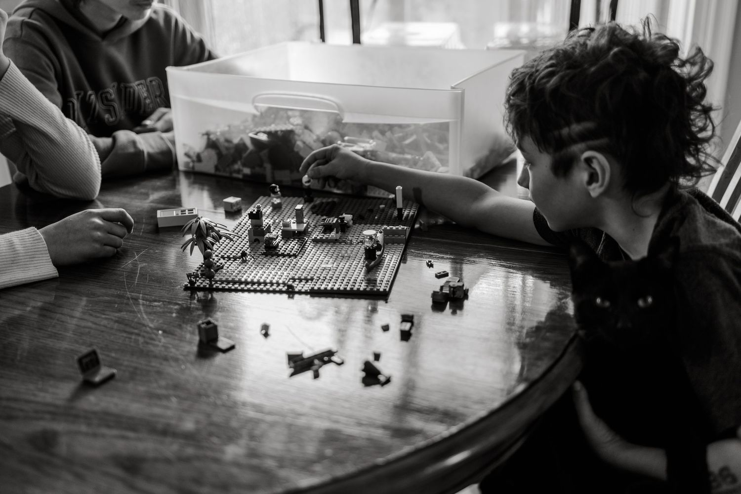 Two children playing with Lego bricks on a wooden table in a black and white photo.