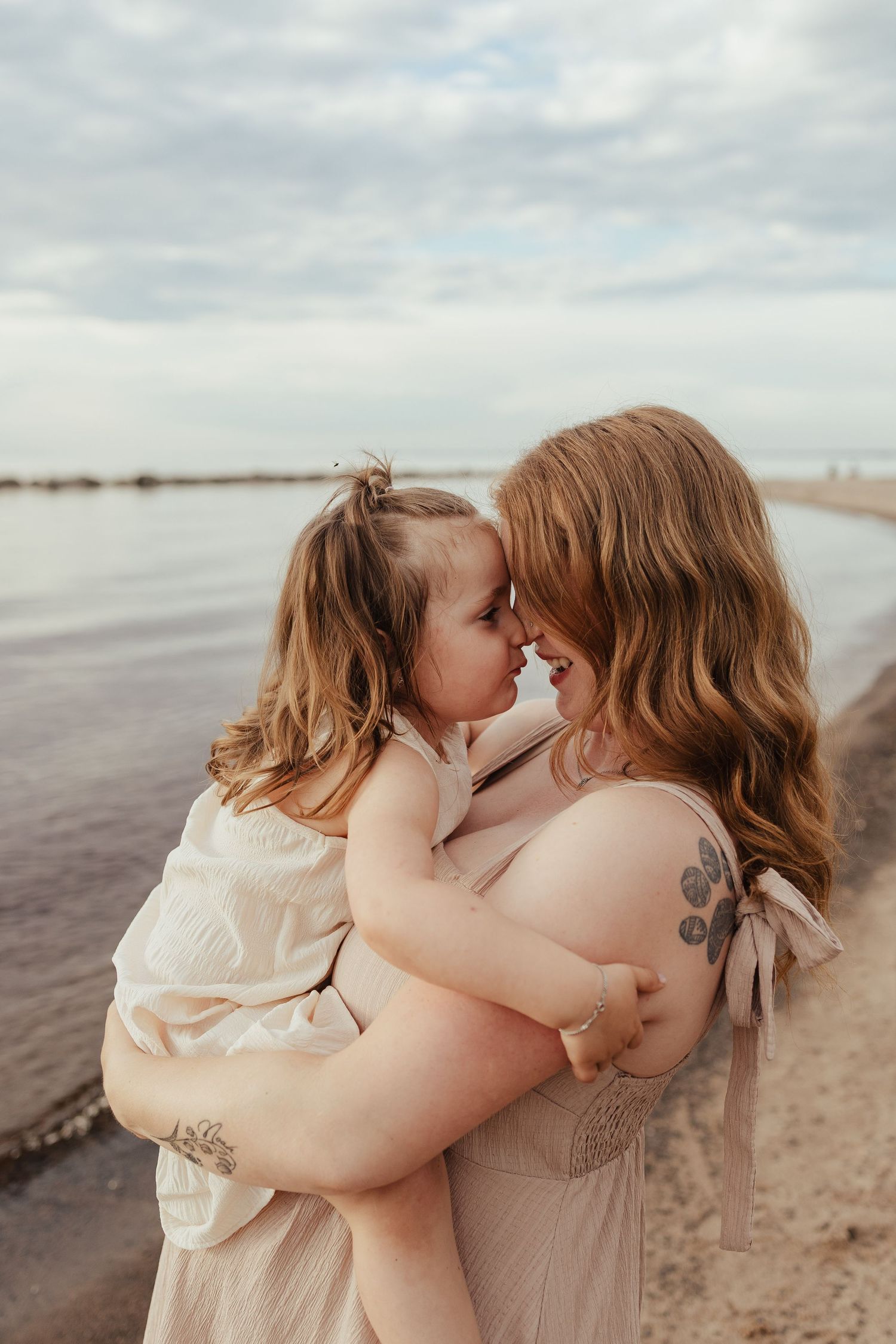 Mother tenderly holding her young daughter face-to-face on a serene beach shoreline.