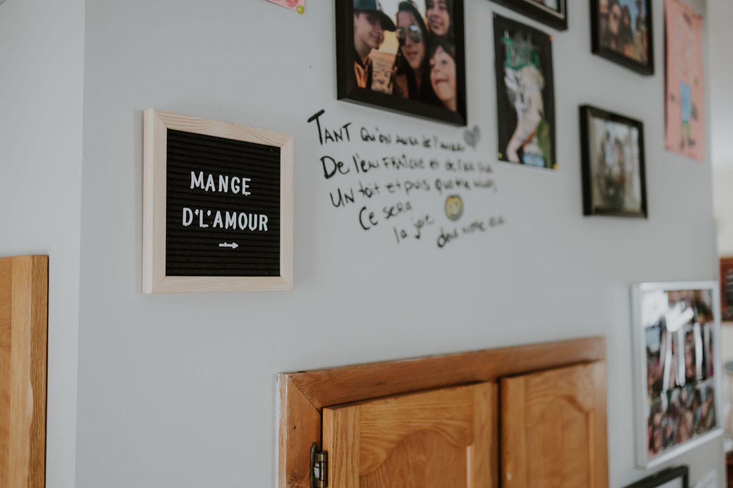 A white wall displays a black letter board reading Mange D'Amour beside handwritten French text and framed family photos.