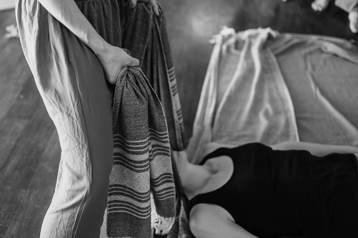 Black and white photo of a massage therapist holding a striped towel near a client lying on a massage table.