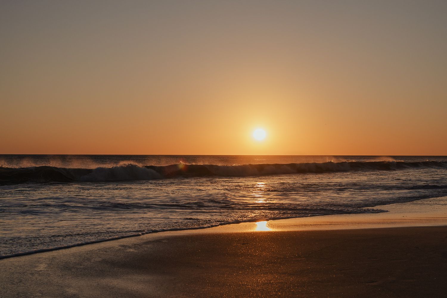 Golden sunset over ocean waves gently washing onto a sandy beach with warm orange sky.