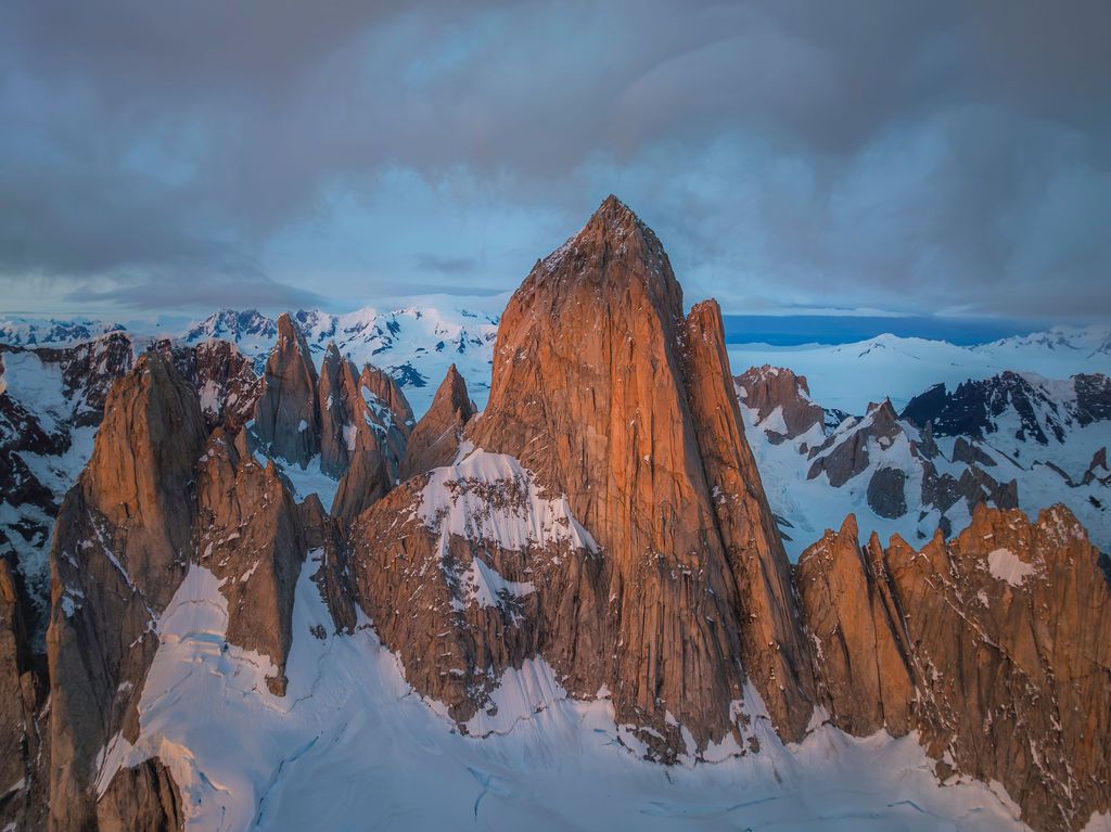 Dramatic aerial view of jagged snow-covered peaks of Mount Fitz Roy at sunset in Patagonia, Argentina.