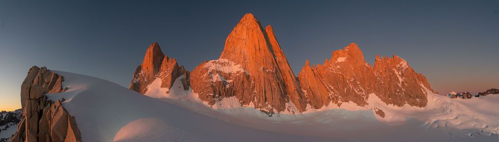 Golden alpenglow illuminates the jagged snow-covered peaks of Cerro Torre at sunrise in Patagonia.