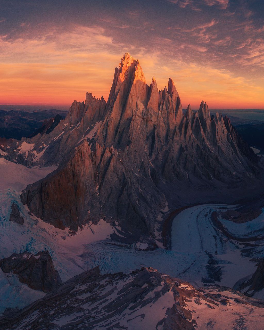Dramatic fiery sunset illuminates jagged Patagonian mountain peaks surrounded by glaciers and snow fields.