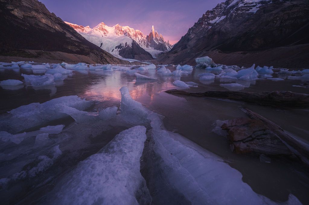 Pink alpenglow on snow-capped peaks reflects in icy glacial lake at dusk in Patagonia.