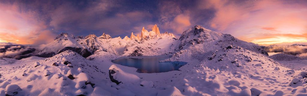 A sweeping winter panorama of snow-covered Patagonian peaks reflected in a frozen lake under a vivid purple sky.