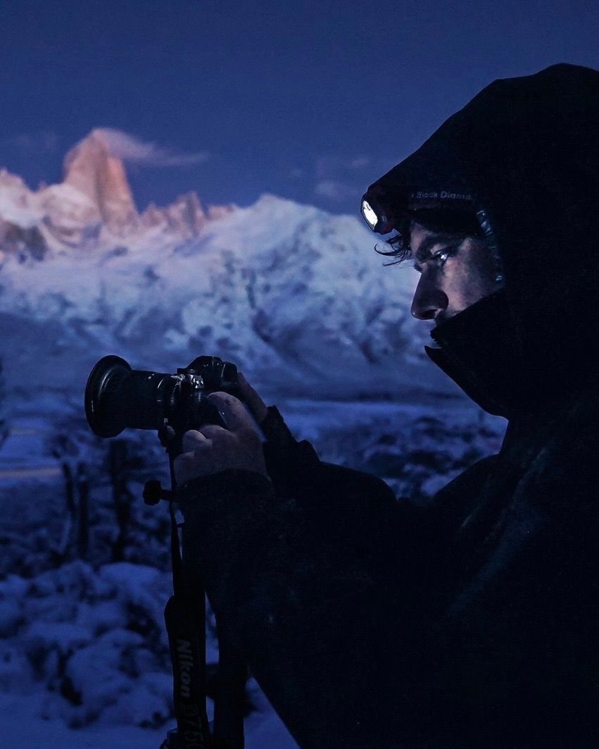 Photographer with headlamp shooting Mount Fitz Roy at blue hour in snowy Patagonia, Argentina.