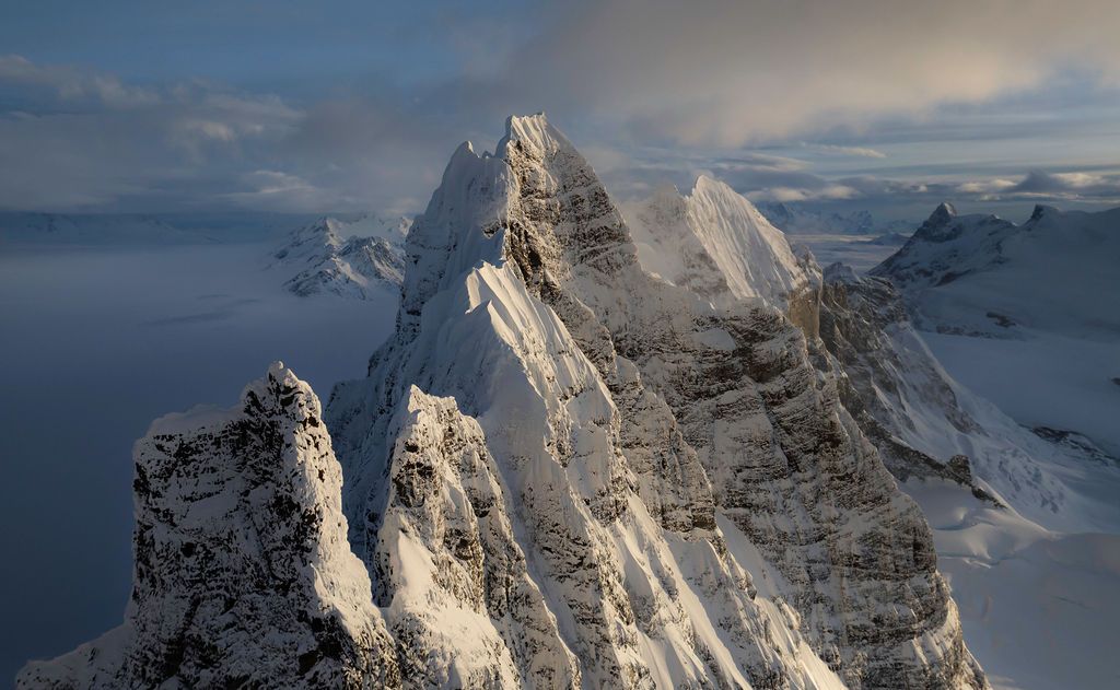 Sharp snow-dusted mountain ridge illuminated by golden light against a moody sky in a remote wilderness.