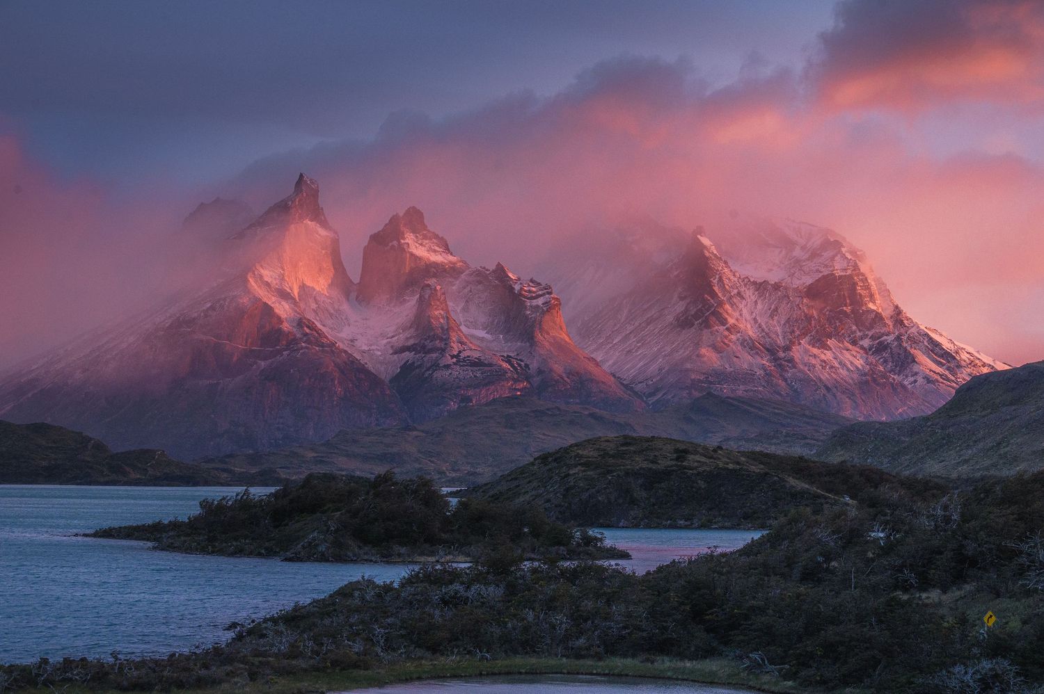 Pink alpenglow illuminates the jagged peaks of Torres del Paine at sunset, reflected in a serene Patagonian lake below.