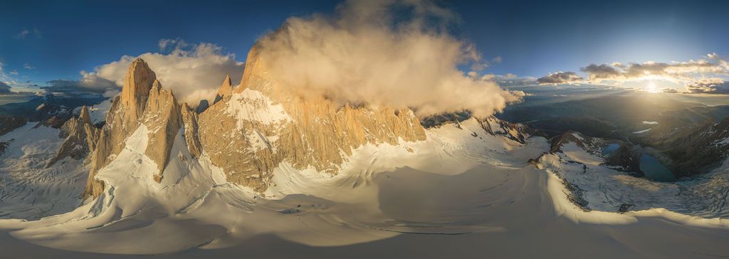 Wide aerial panorama of Patagonia's Torres del Paine massif bathed in warm golden sunset light over snow.