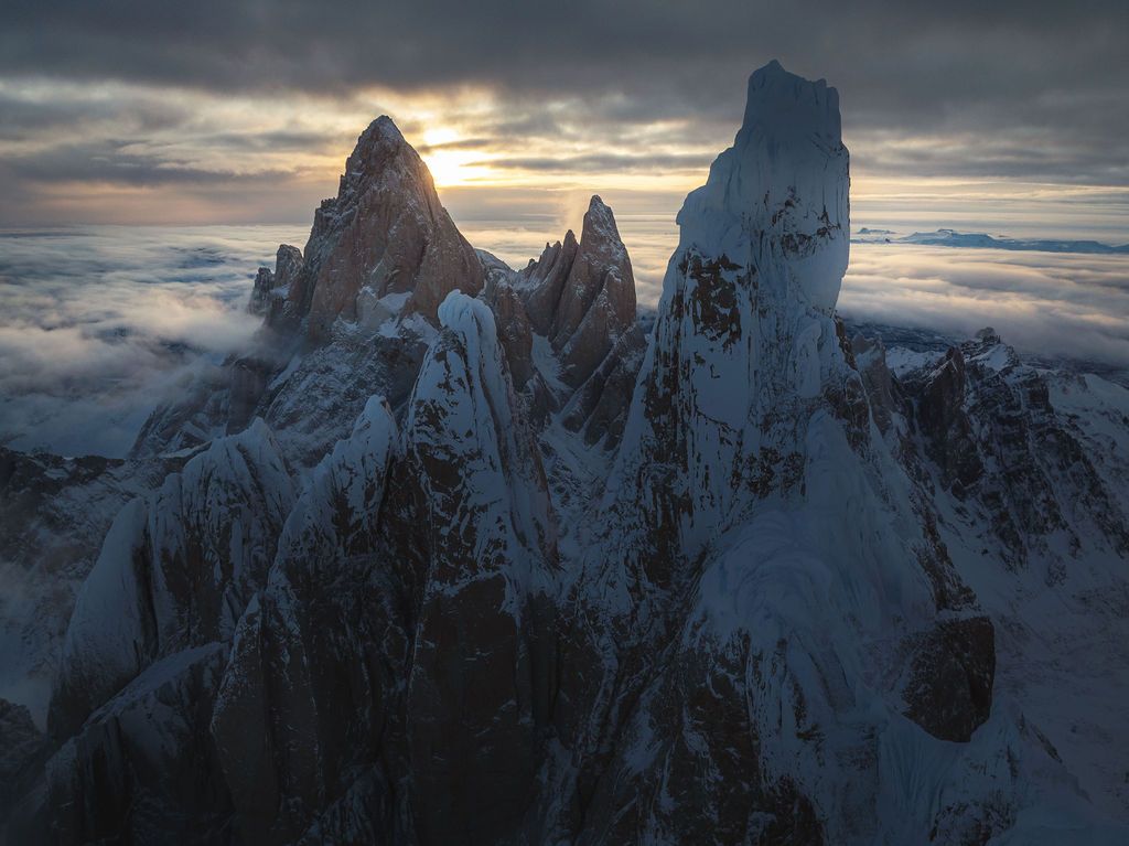 Snow-dusted jagged mountain peaks emerge from a sea of clouds at moody twilight in Patagonia.