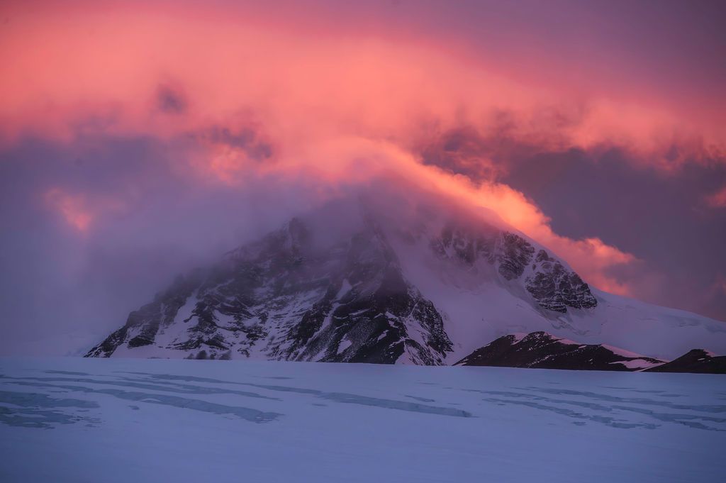 A snow-covered Patagonian mountain peak shrouded in glowing pink storm clouds at dramatic sunset.