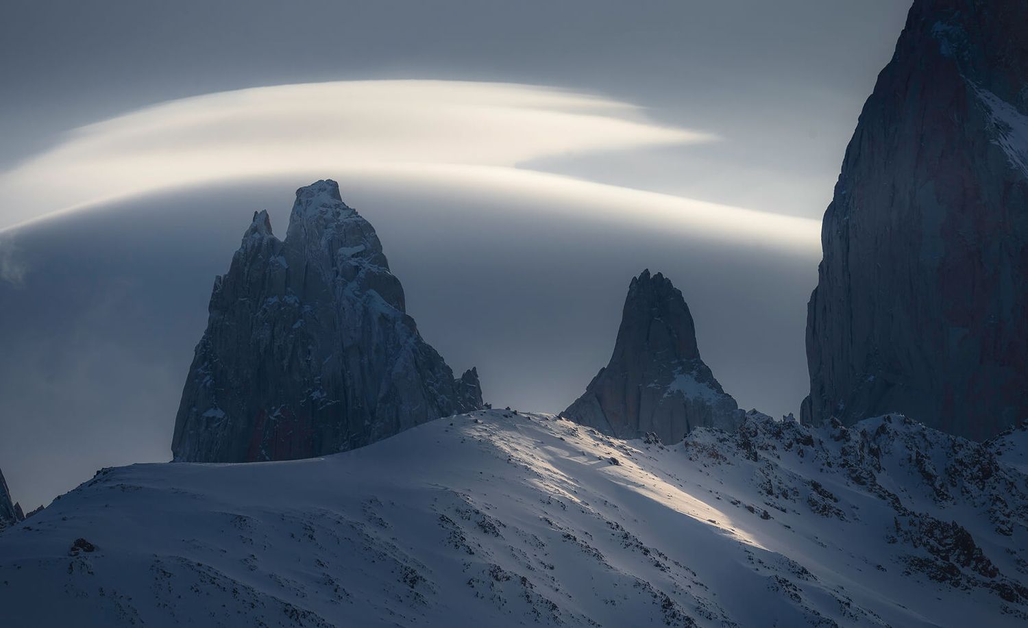 Dramatic lenticular clouds swirl over jagged snow-covered peaks in Torres del Paine, Patagonia.