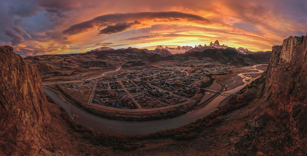 Dramatic sunset panorama over El Chalten town with Fitz Roy mountain visible under fiery cloudy skies.