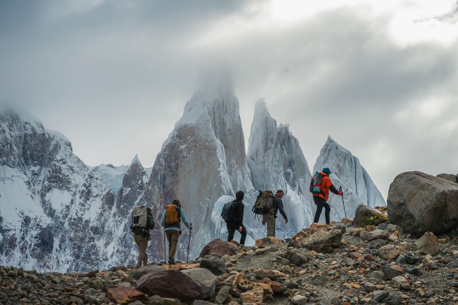 Group of hikers with backpacks trekking toward the dramatic spires of Cerro Torre in Patagonia.