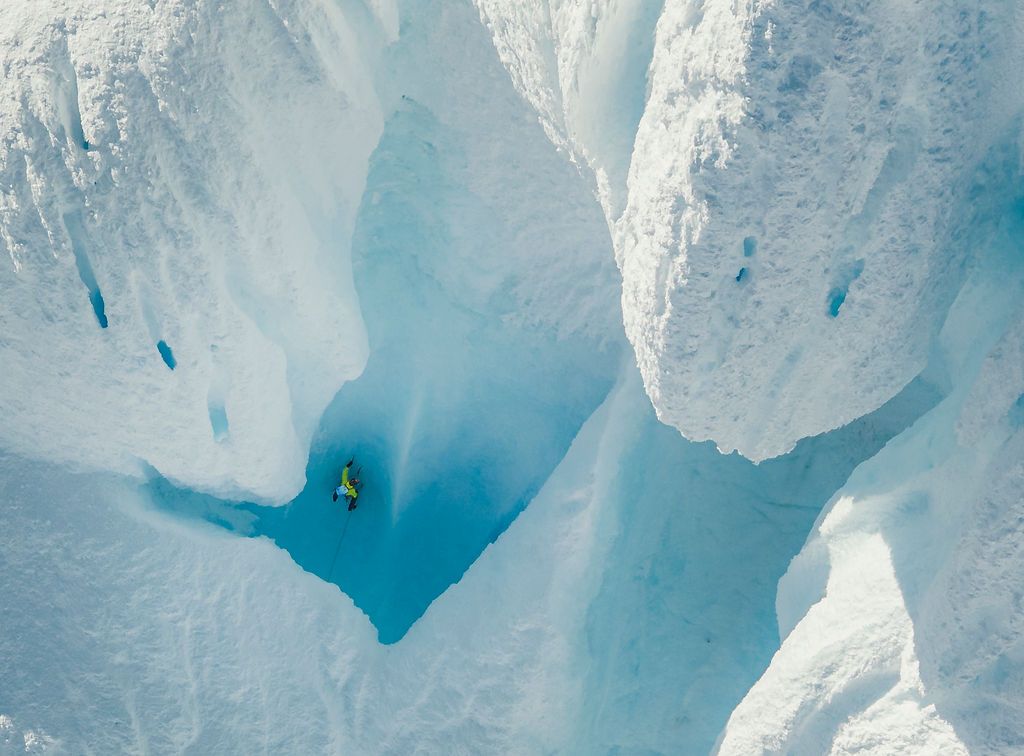 Aerial view of climber nestled in a deep blue glacial crevasse surrounded by white ice walls.