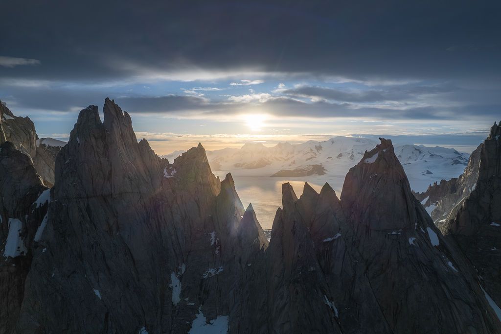 Moody aerial view of sharp rocky pinnacles silhouetted against a glowing sunset sky in Patagonia.