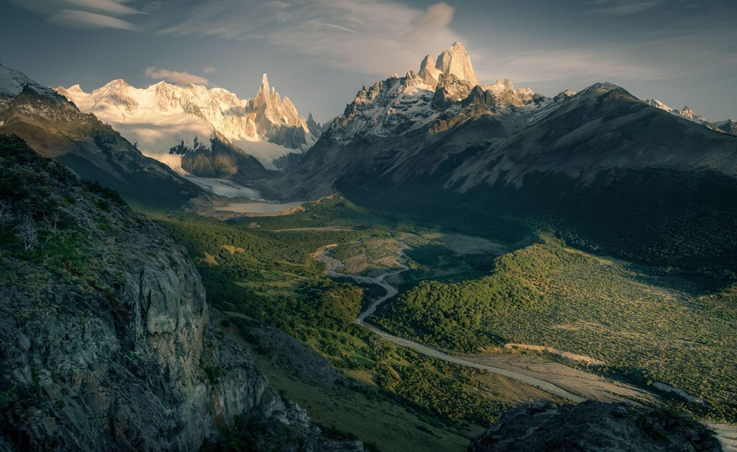 Panoramic aerial view of Cerro Torre and Fitz Roy massif over lush green valley in Patagonia.