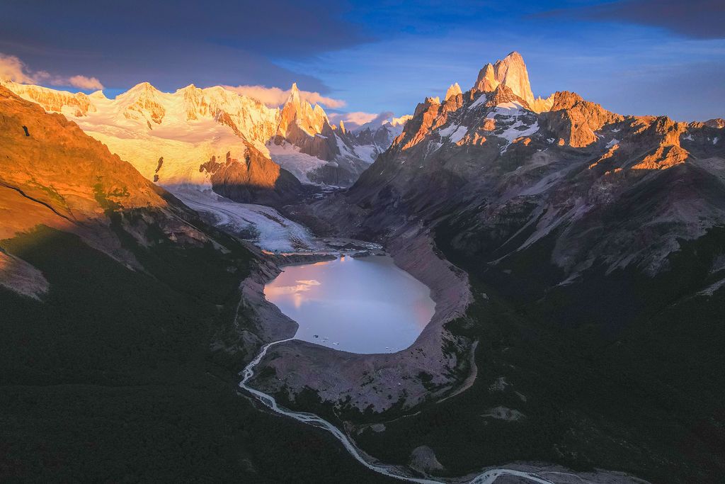 Golden sunrise illuminates Mount Fitz Roy and a frozen glacial lake surrounded by Patagonian wilderness.