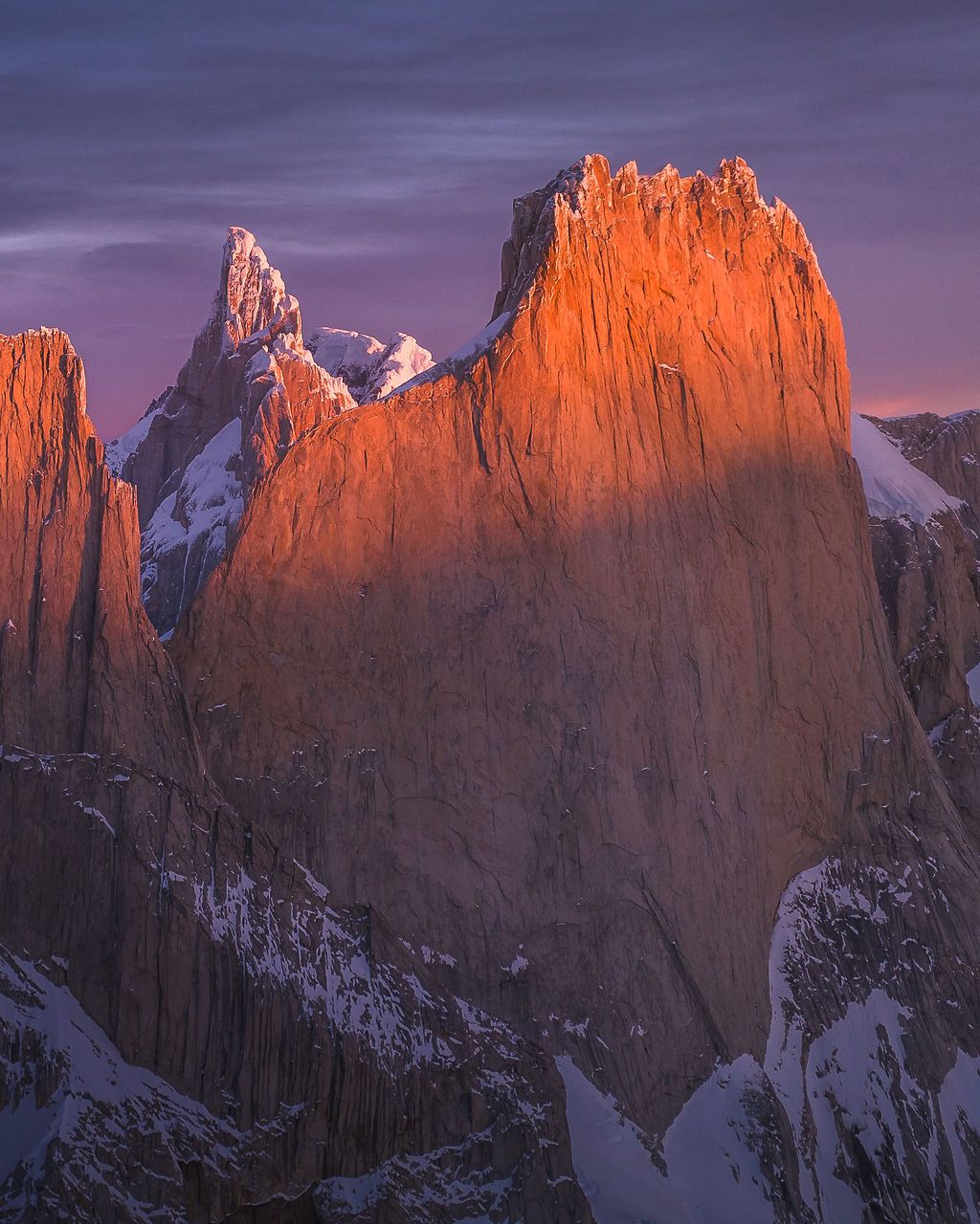 Towering granite walls of Patagonia's Cerro Torre massif illuminated by vivid orange alpenglow at sunset.