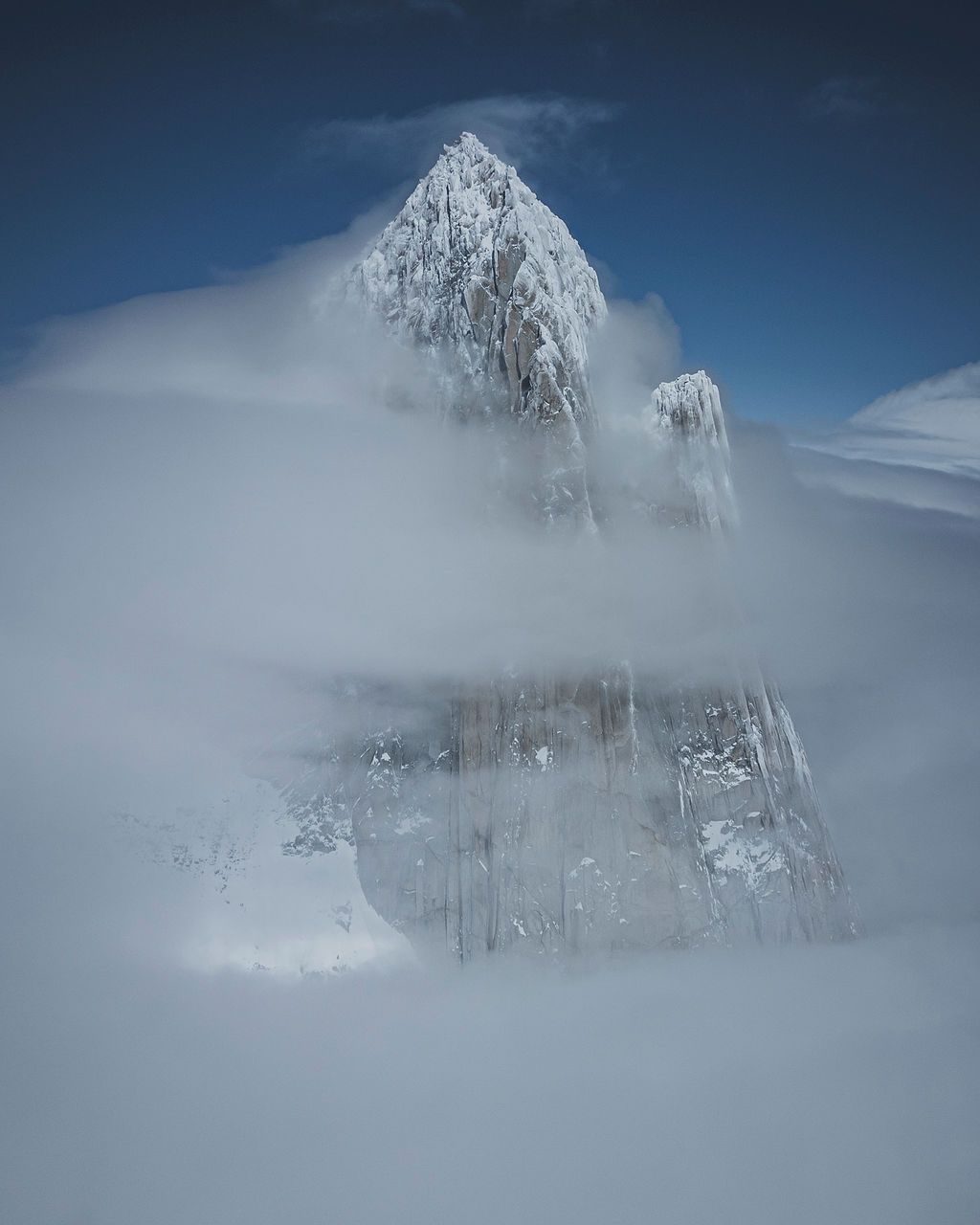 Cerro Torre mountain peak dramatically shrouded in blizzard snow and thick white clouds in Patagonia.
