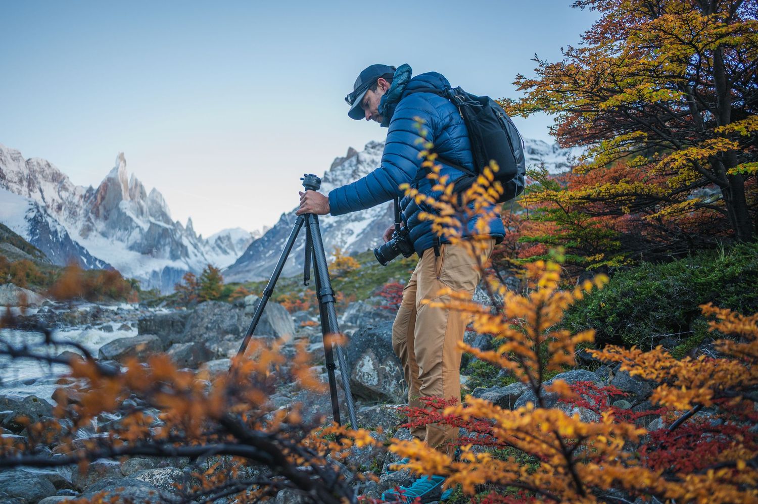 Photographer on tripod capturing Cerro Torre mountain peak surrounded by colorful autumn foliage in Patagonia.