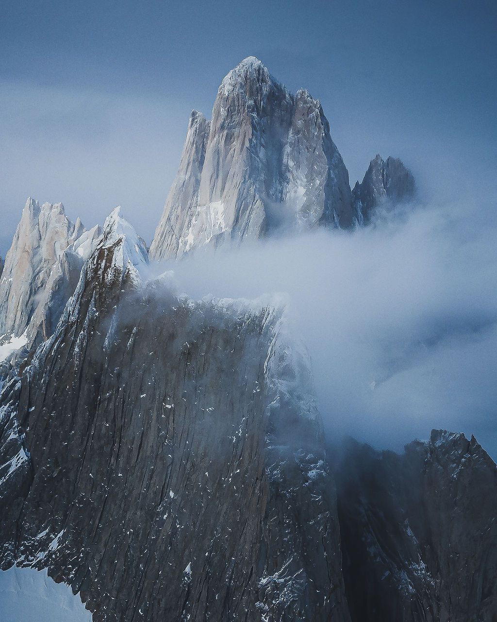 Cerro Torre granite spire emerging through swirling mist and clouds in Patagonia's dramatic mountain landscape.