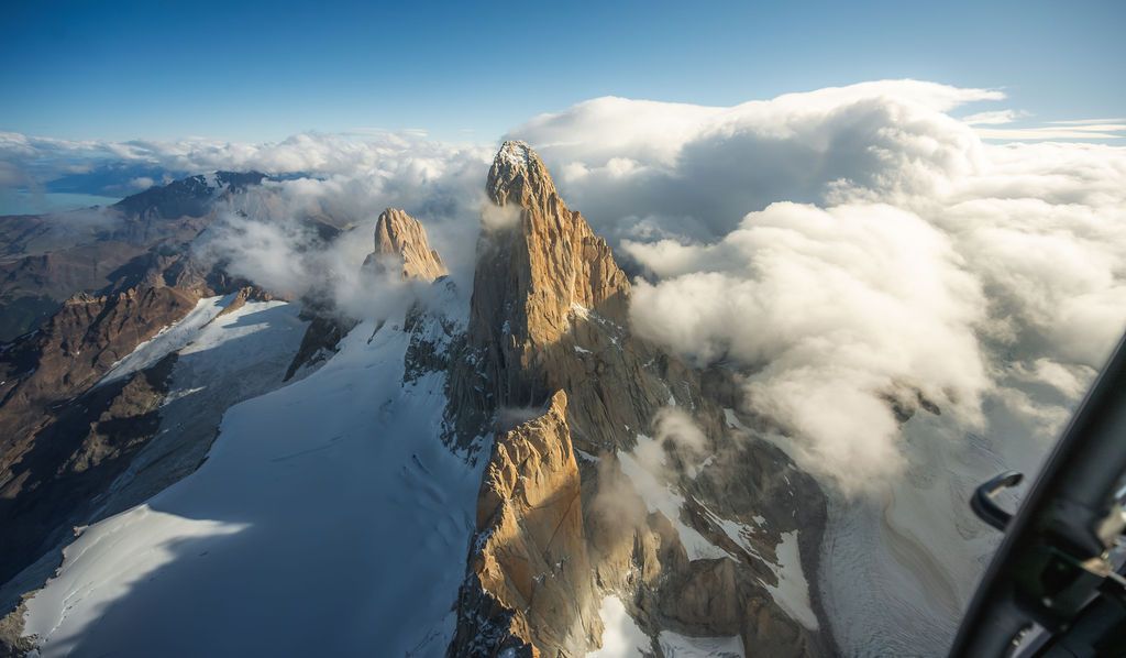 Aerial helicopter view of rugged granite towers and glaciers emerging through clouds in Patagonia on a clear day.