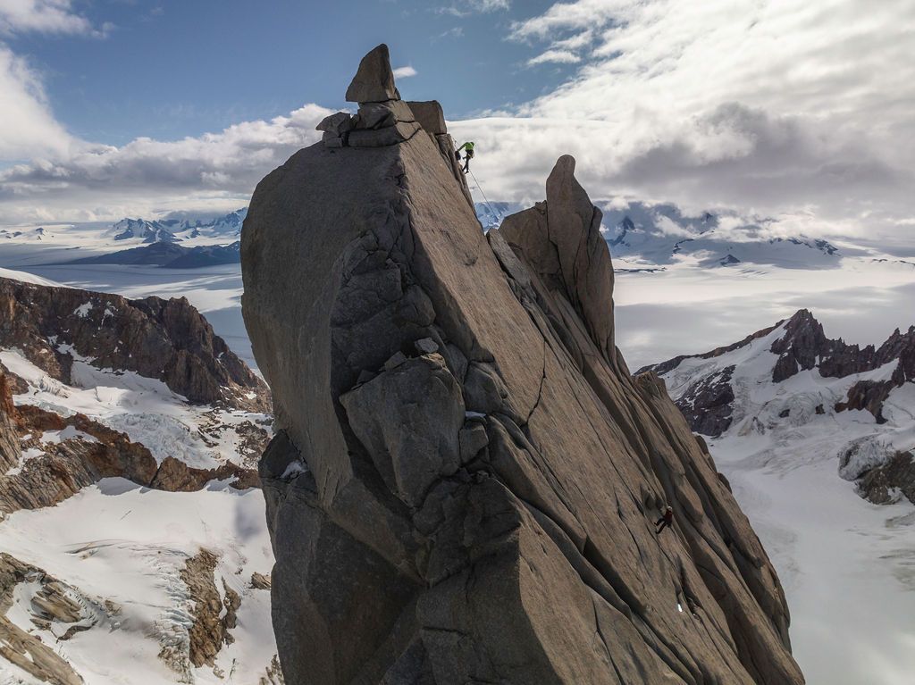 Two climbers traverse a narrow rocky ridge with vast Patagonian ice fields and mountains stretching behind.