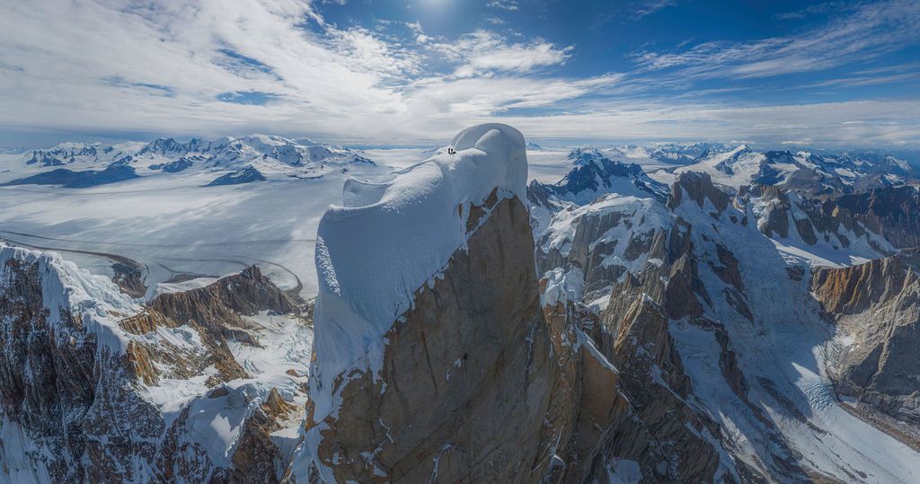 Aerial view of a sharp rocky summit surrounded by vast snow-covered glaciers and mountain ranges in Patagonia.