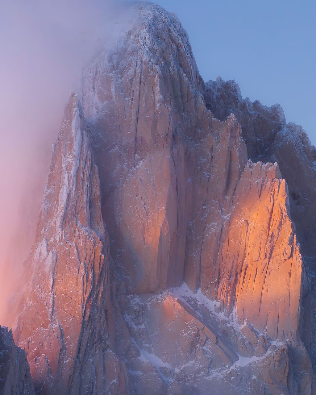 Close-up of jagged granite peaks glowing orange at sunset with misty clouds swirling around the rocky spires.