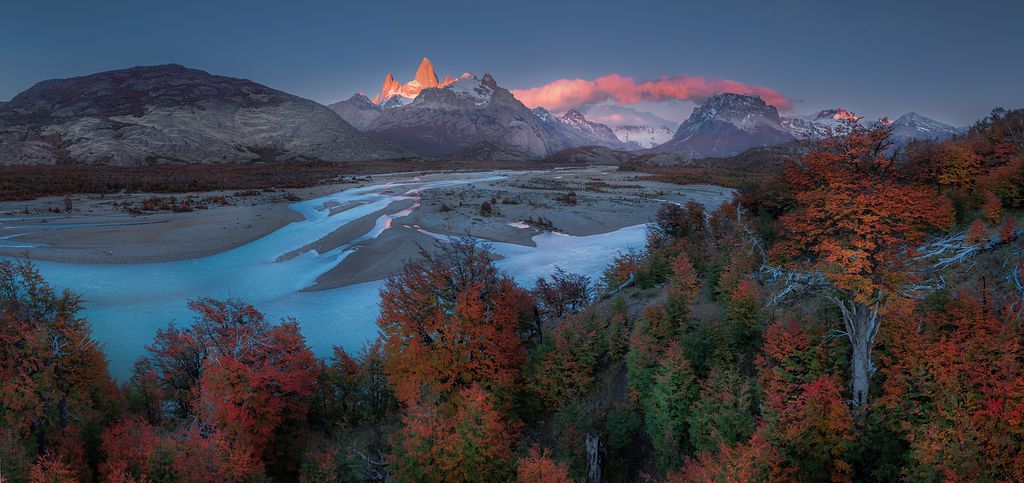Panoramic autumn landscape with colorful foliage along a turquoise river with Fitz Roy glowing at sunrise.