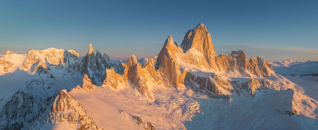 Golden sunrise illuminates the iconic jagged peaks of Fitz Roy and Cerro Torre in Patagonia, Argentina.