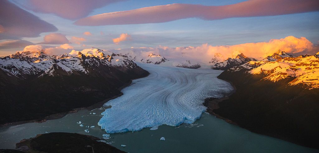 Aerial panorama of a massive glacier flowing into turquoise waters at sunset in Patagonia.