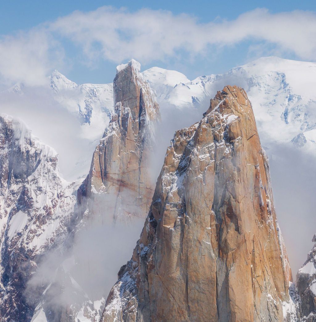 Two rugged brown rock spires dusted with snow rise above misty clouds in a mountain range.