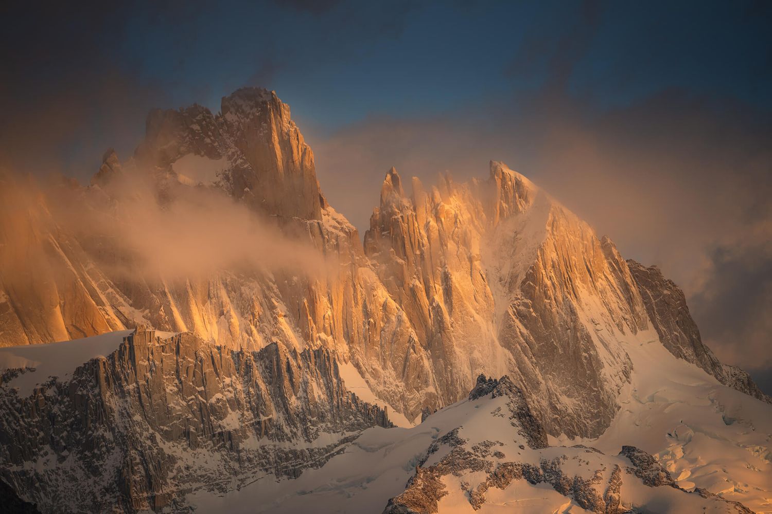 Fiery golden sunset illuminates the rugged snow-capped granite peaks of Mount Fitz Roy in Patagonia.