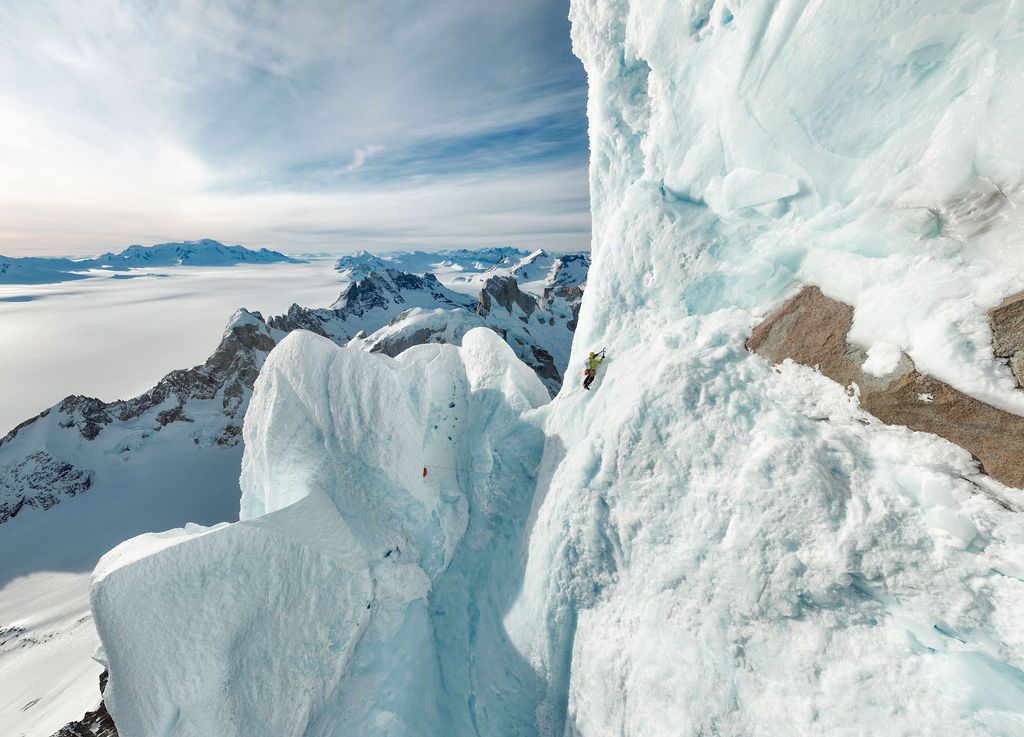 Climber ascending jagged ice formations on a high-altitude ridge with vast frozen landscape below.