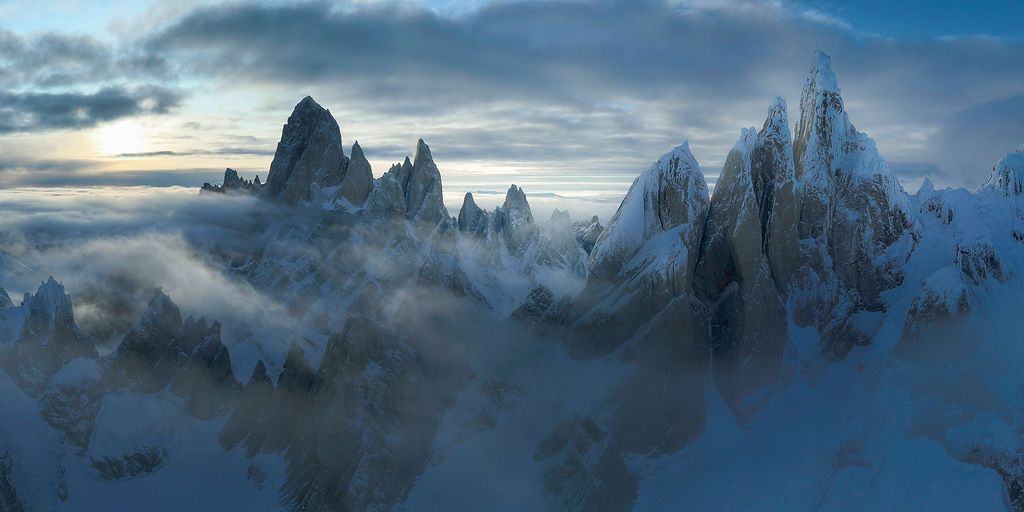 Misty aerial view of snow-covered Fitz Roy and Cerro Torre peaks shrouded in clouds at dusk in Patagonia.