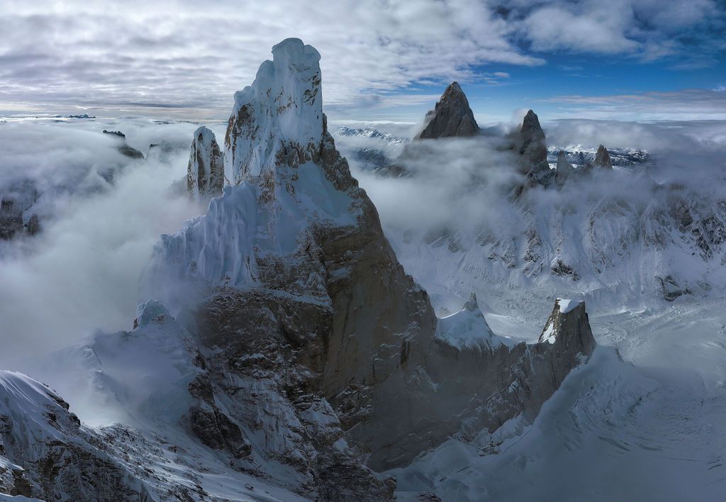 Aerial view of ice-covered granite towers of Mount Fitz Roy emerging through swirling clouds in Patagonia.