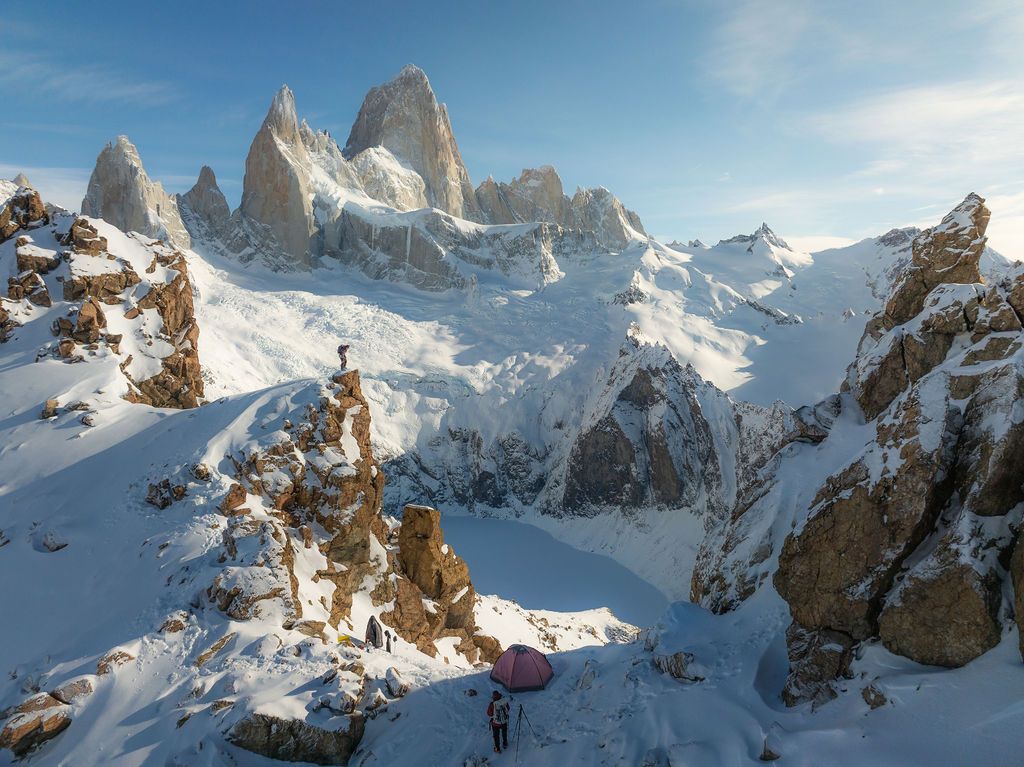 Mountaineers camp below the iconic granite spires of Fitz Roy massif in a vast snowy Patagonian landscape.