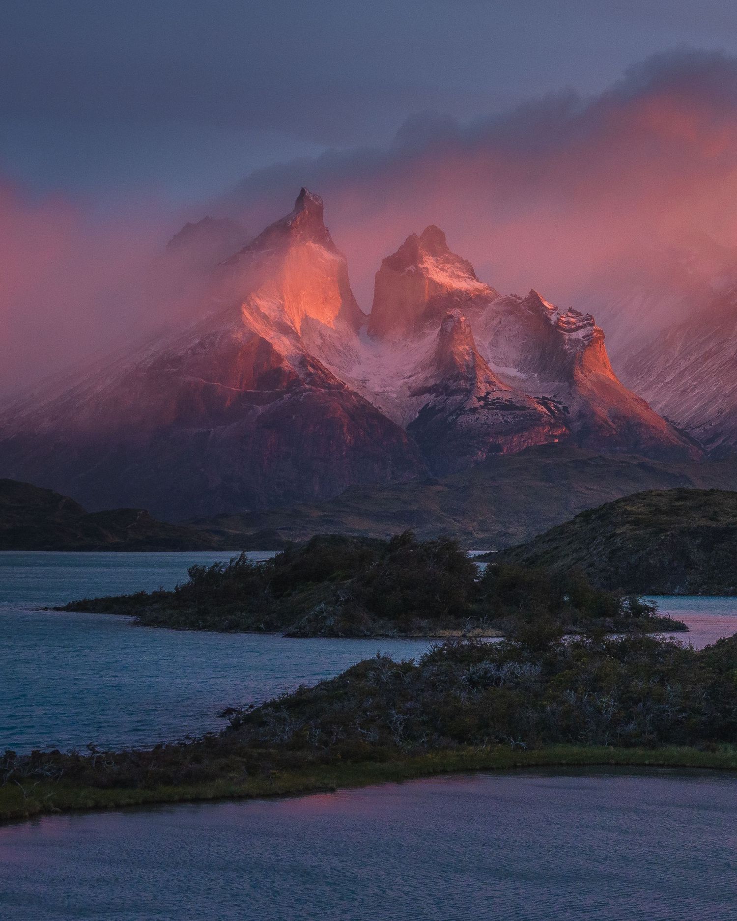 Dramatic pink and red alpenglow illuminates the jagged peaks of Torres del Paine at sunset, reflected in a serene Patagonian lake.