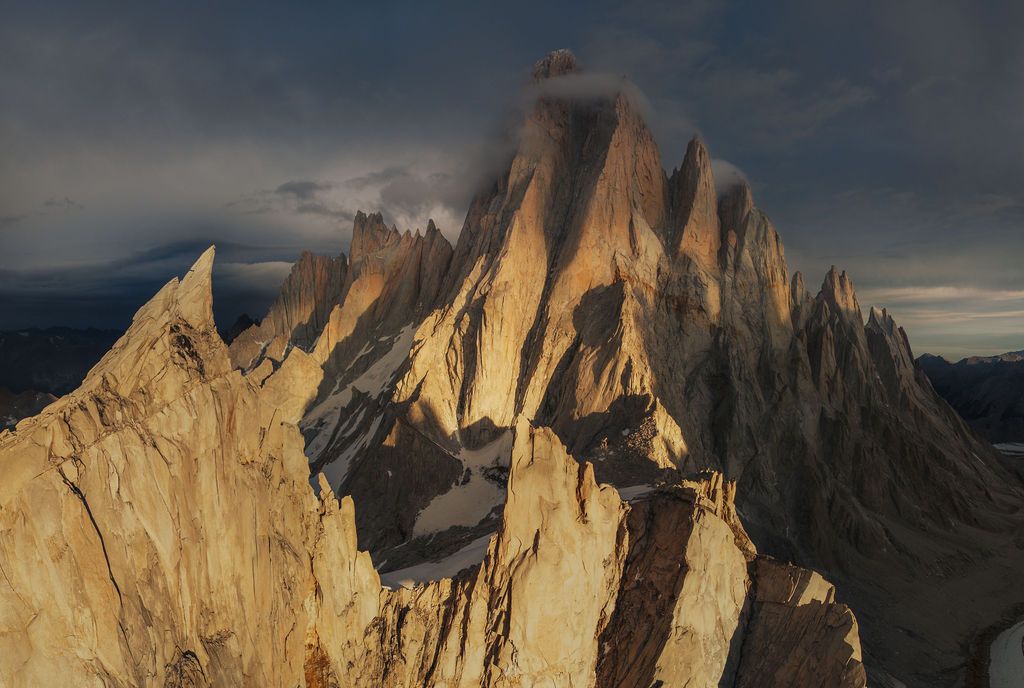Aerial view of jagged granite peaks of Cerro Torre at golden hour with dramatic storm clouds in Patagonia.