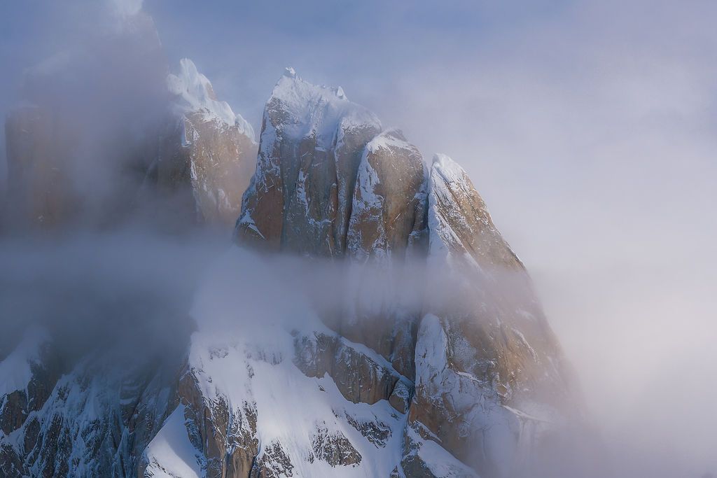 Snow-covered granite rock towers emerge dramatically through thick swirling mountain fog.