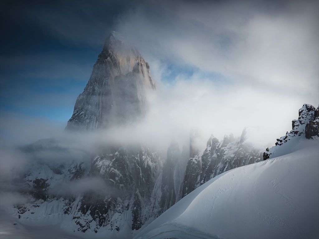 Jagged mountain peak partially obscured by thick rolling fog and snow in a dramatic moody winter landscape.