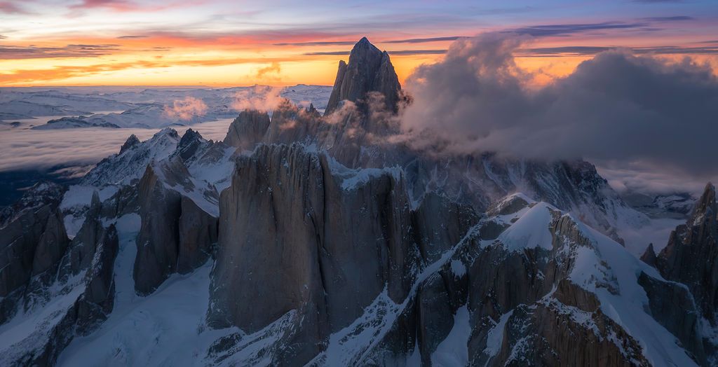 Dramatic aerial view of jagged snow-covered peaks of Fitz Roy at fiery sunset in Patagonia.