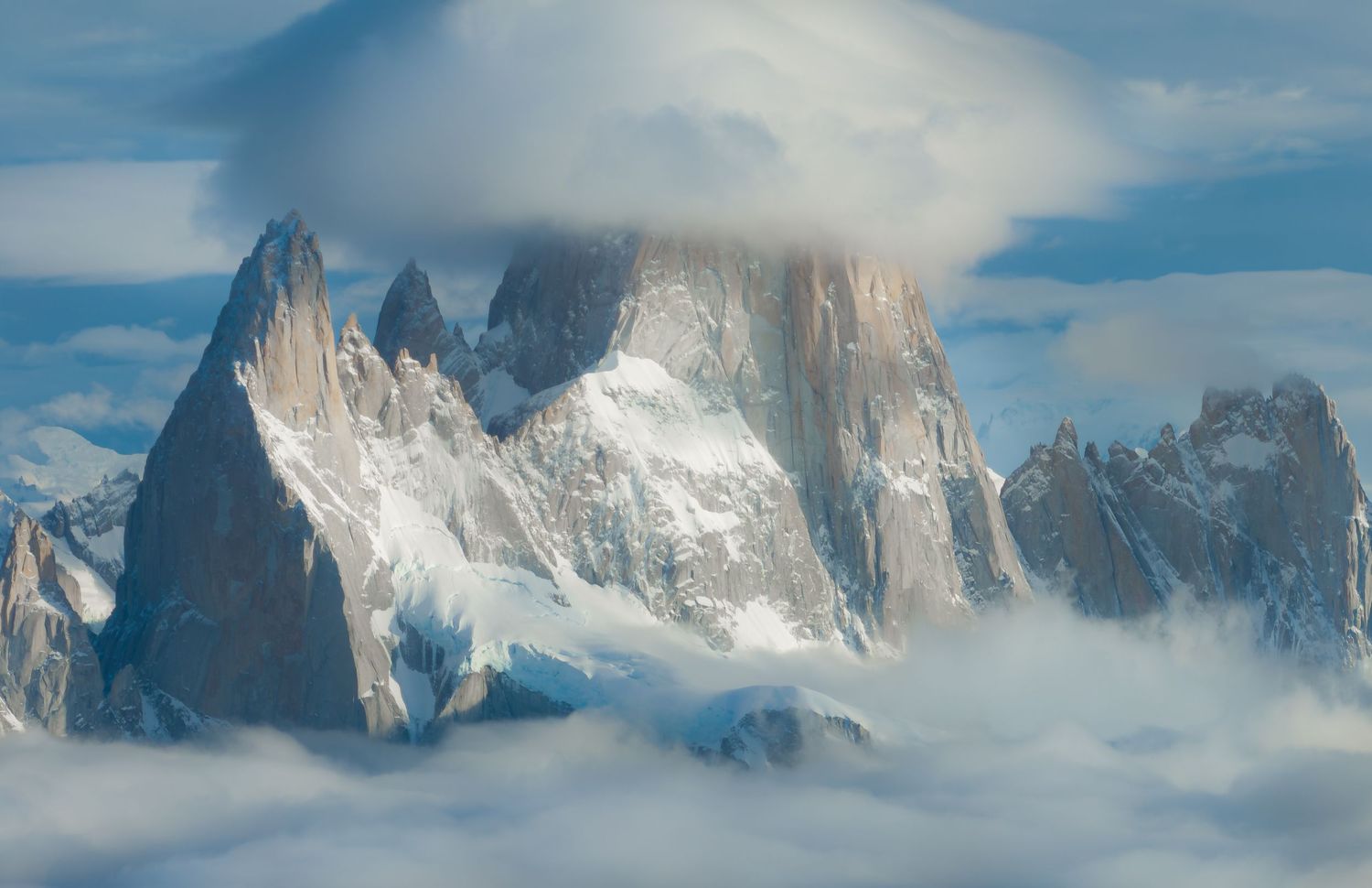Snow-capped mountain peaks piercing through clouds in Patagonia, with dramatic rocky spires rising above a sea of mist.
