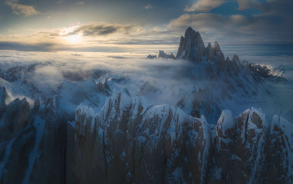 Ethereal aerial view of Mount Fitz Roy rising above a sea of mist and jagged peaks at sunrise.