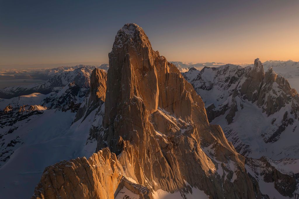 Warm golden sunset light bathes the iconic granite spire of Monte Fitz Roy above snowy glaciers.