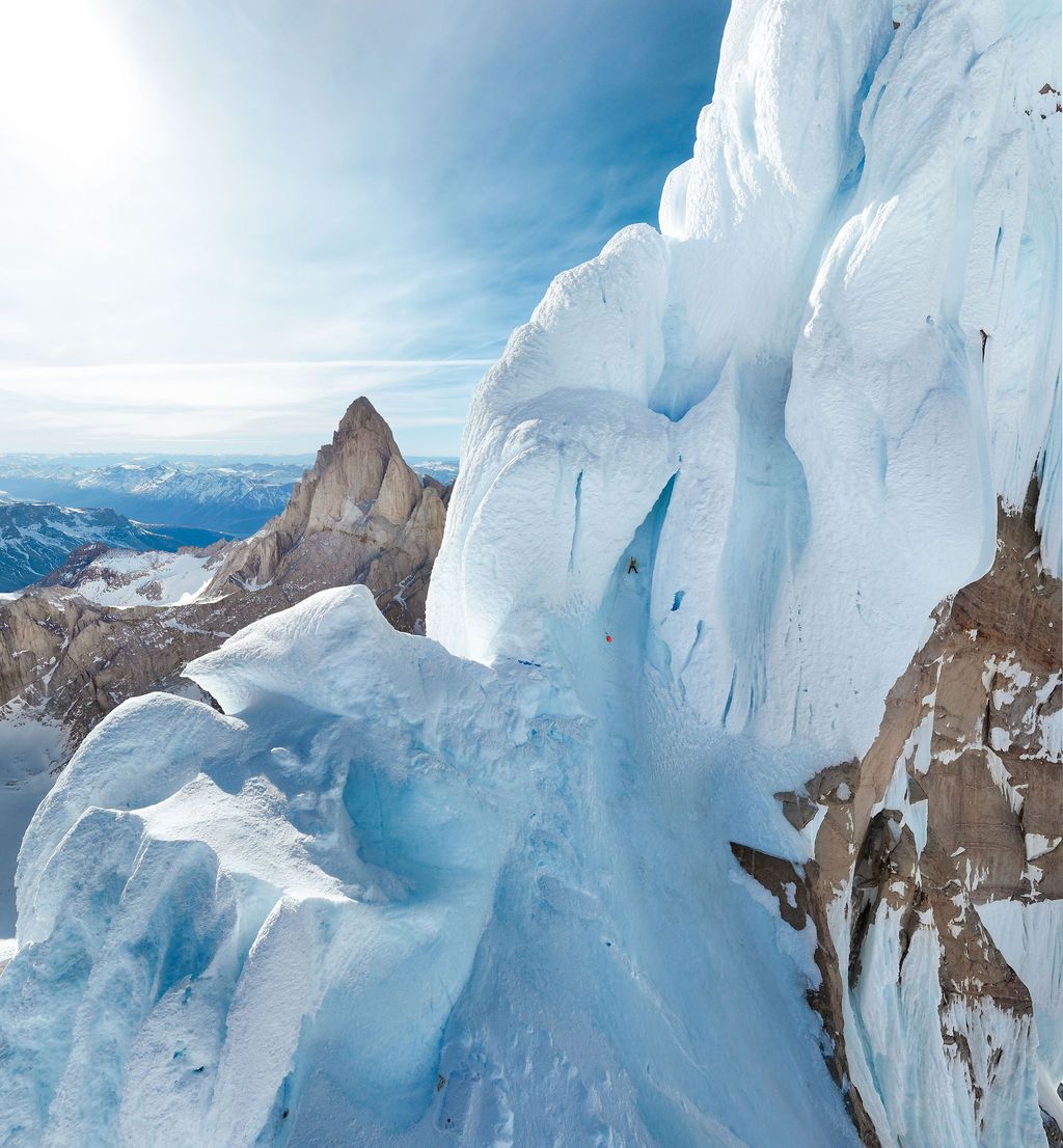 Close-up of dramatic glacier ice formations on a mountain ridge with rocky peaks and blue sky in Patagonia.