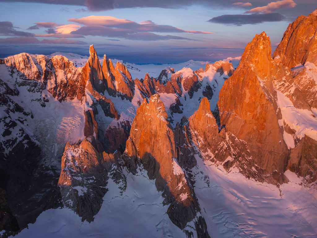 Stunning aerial sunset view of snow-covered Cerro Torre massif glowing orange in Patagonia, Argentina.